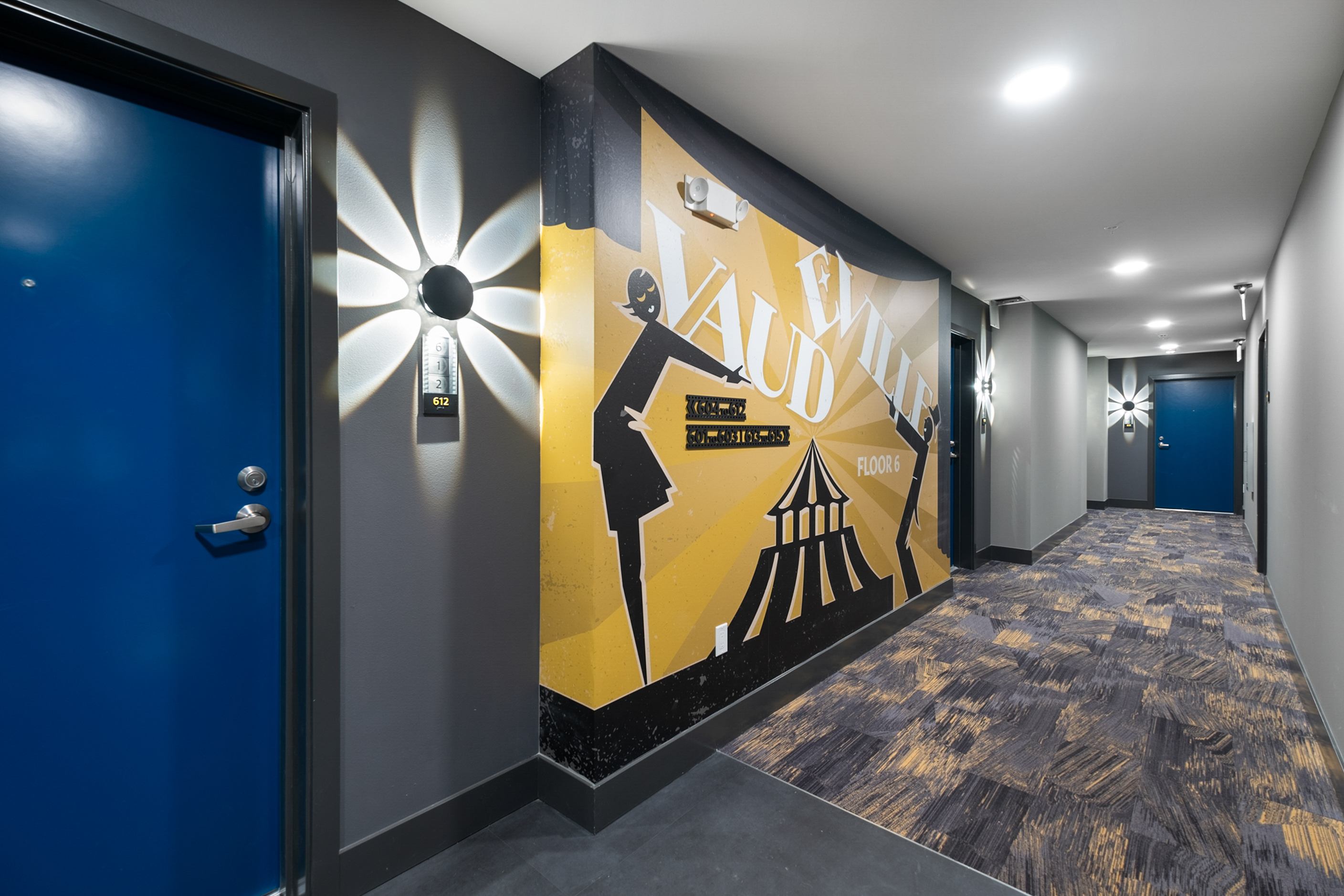 A hallway with a blue door and a yellow wall with a woman on it.